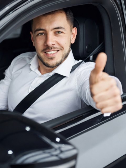 Șofer în cămașă albă la volan, cu degetul mare ridicat