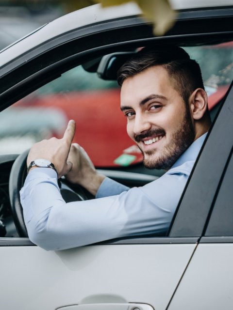 Șofer zâmbitor în cămașă albastră, la volan