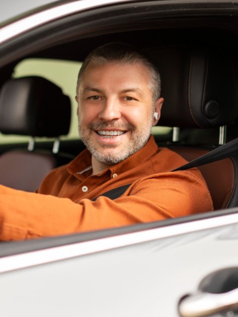 Șofer zâmbitor în cămașă portocalie, la volan
