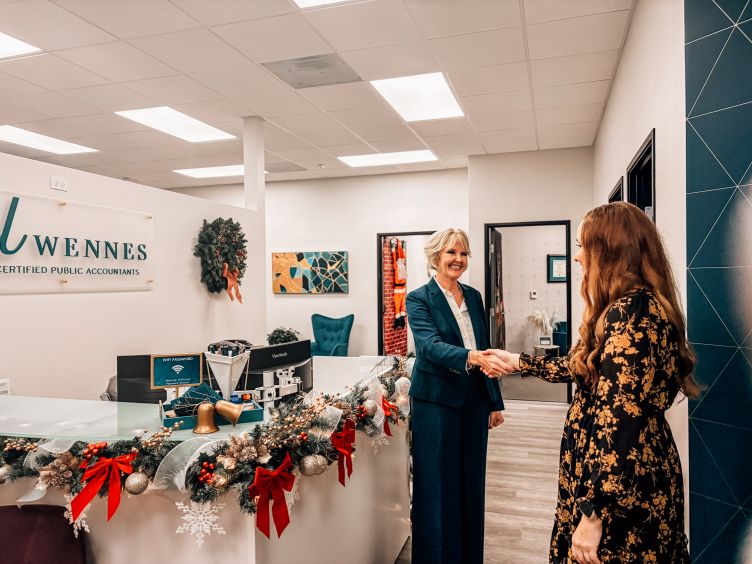 Two women having a conversation indoors, one holding folders and smiling, the other facing away from the camera.