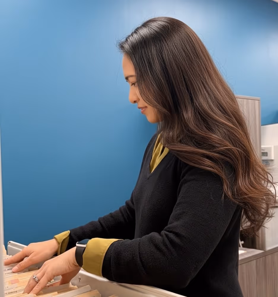 Person sorting or searching through labeled files in a filing cabinet drawer.