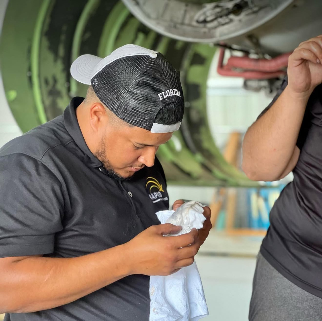 Man in a black shirt and black-and-white cap looking down while holding a white cloth.