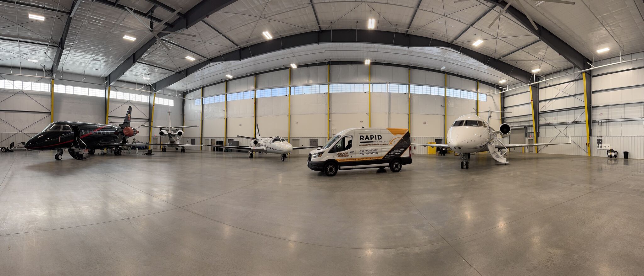 Interior of a large aircraft hangar with three private jets and a repair service van parked inside.