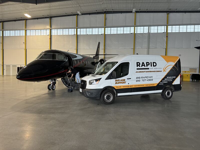 White Rapid AOG Services van parked inside an aircraft hangar next to a black private jet with a person attending to the jet's open cargo hatch.