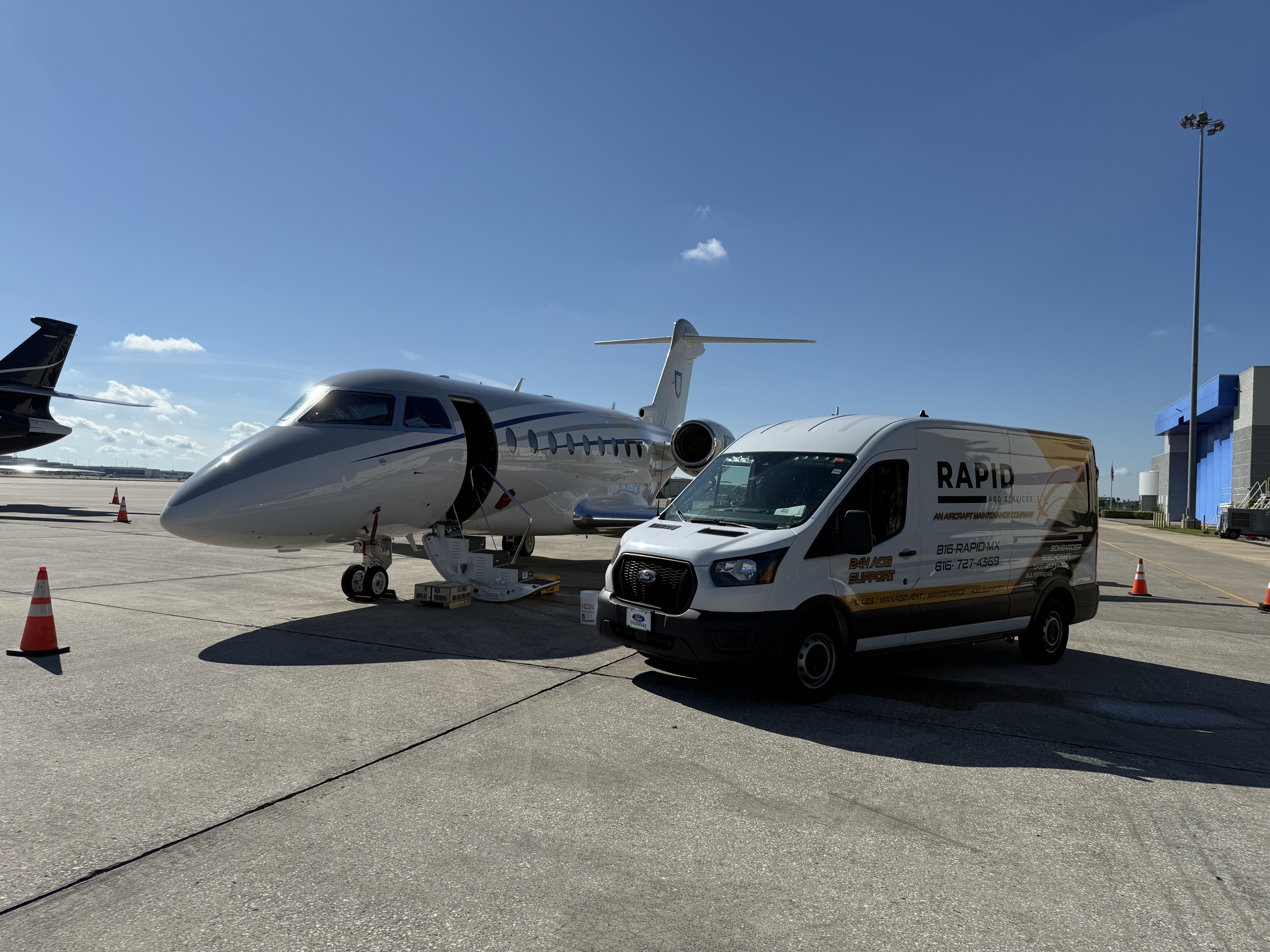 Private jet on tarmac with open door and stairs, next to a Rapid AOG Services maintenance van under clear blue sky.