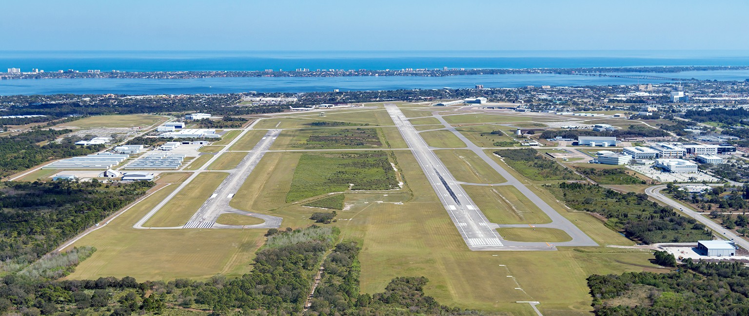 Aerial view of an airport with two parallel runways, adjacent taxiways, and surrounding green areas.