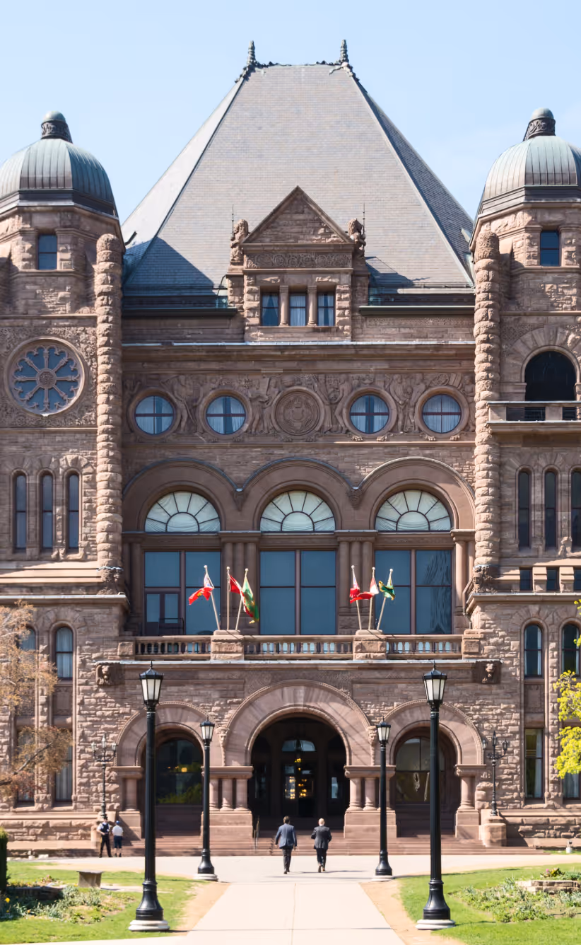 Front view of a historic stone government building with arched entrances, flagpoles, and decorative windows under a clear sky.