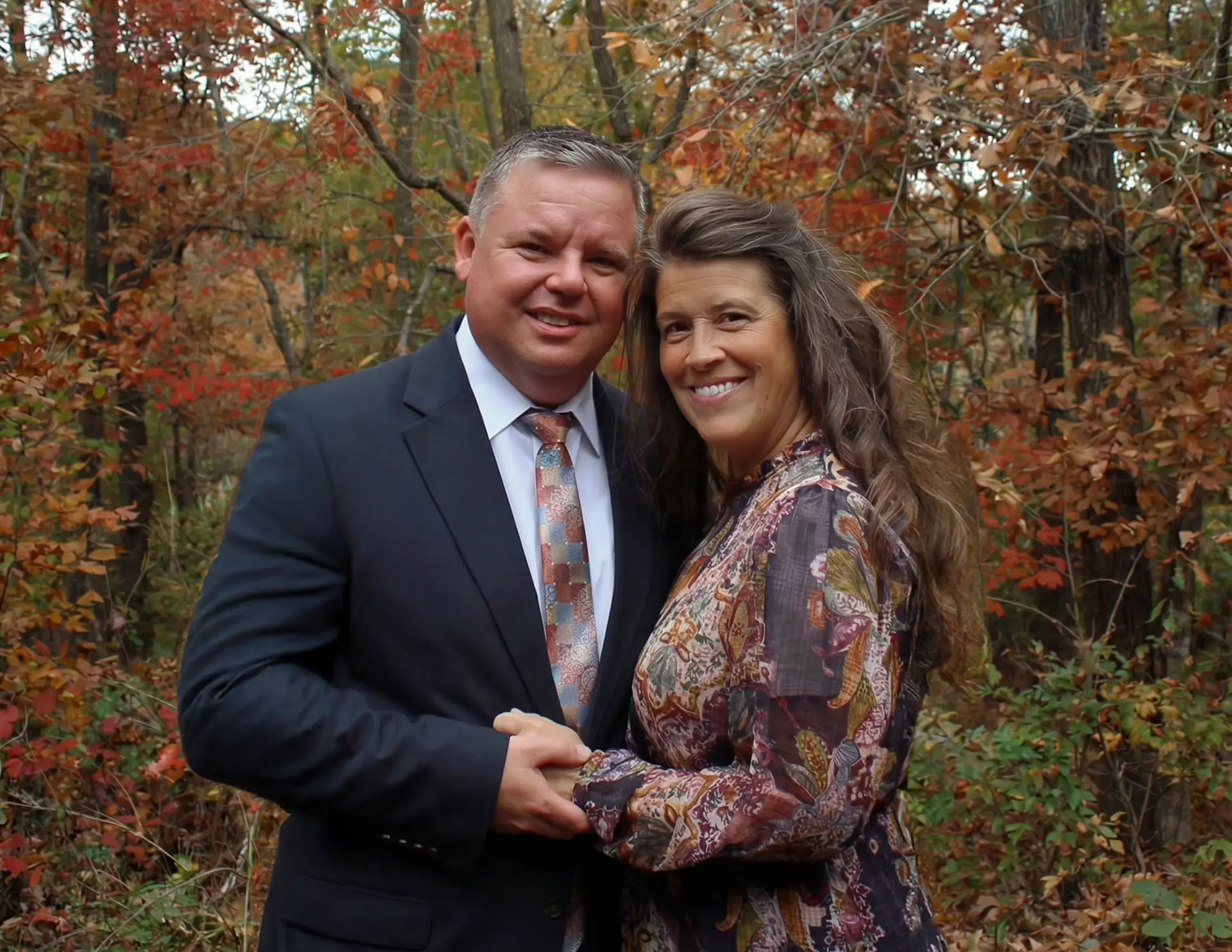 Couple smiling and holding hands in an autumn forest with colorful fall leaves.