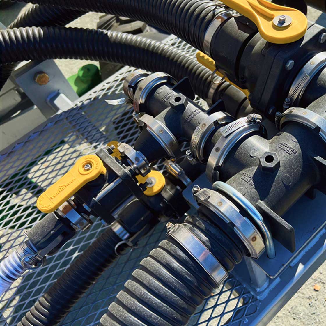 Black industrial pipes with yellow valve handles and metal clamps mounted on a metal grated platform.