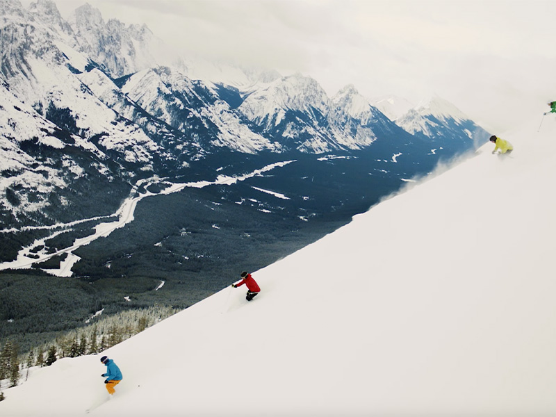 People skiing down Nakiska with a mountain view