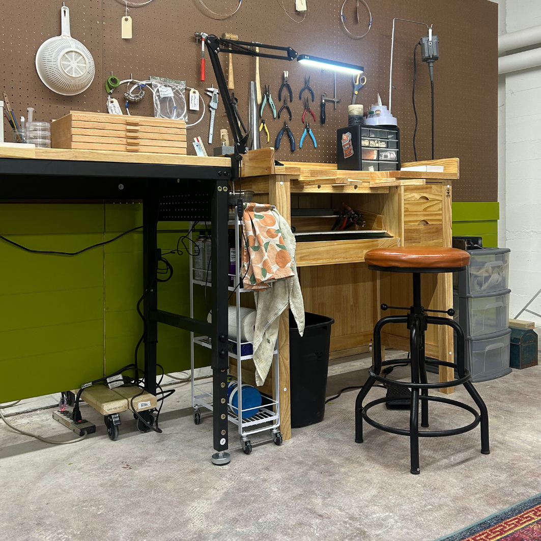 A tidy workspace with wooden workbench, hanging tools on pegboard, a lamp, and a rolling chair with a brown seat.