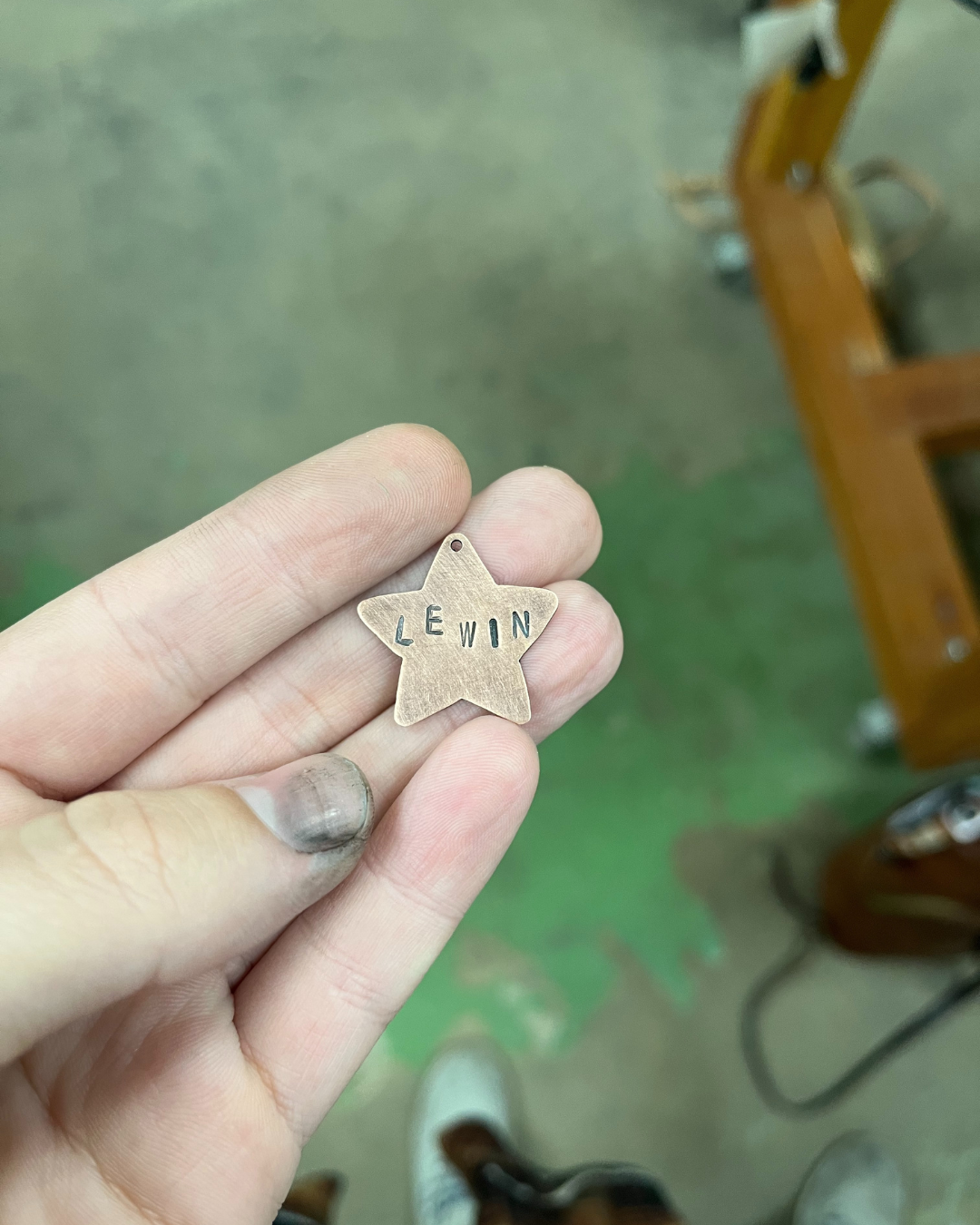 Hand holding a small star-shaped metal tag engraved with the name "LEWIN".