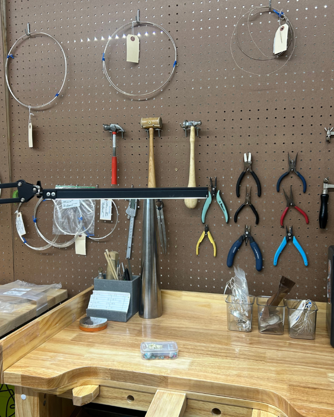 Workbench with a pegboard holding various hand tools including hammers, pliers, wire cutters, and coiled wires with tags.