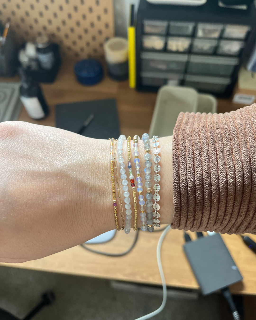 Close-up of a wrist wearing multiple delicate beaded and metal bracelets in gold, white, and translucent tones.