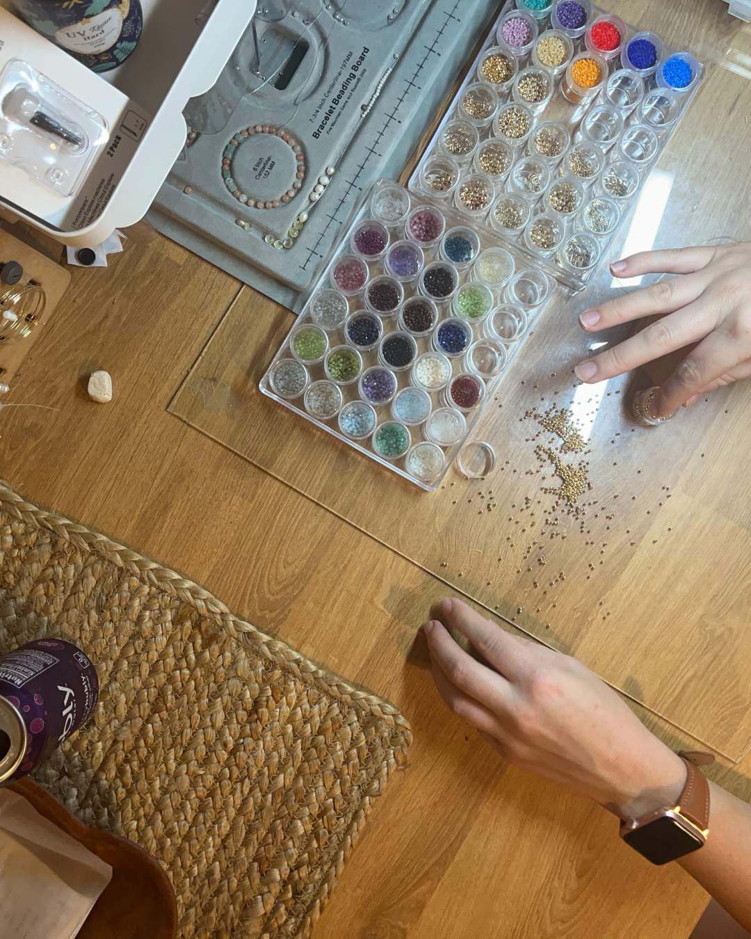 Hands working with small colorful beads and a bracelet beading board on a wooden table.