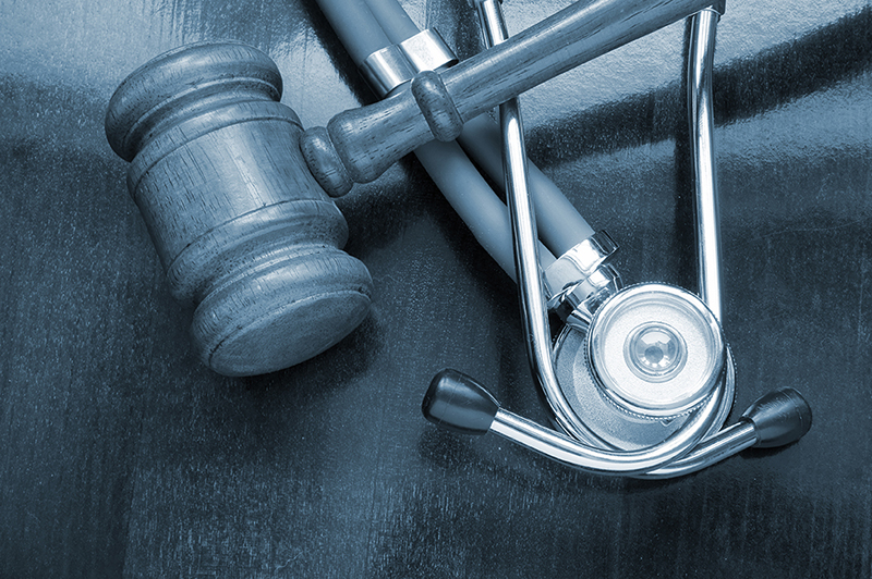 Wooden judge gavel resting next to a stethoscope on a dark wooden surface.