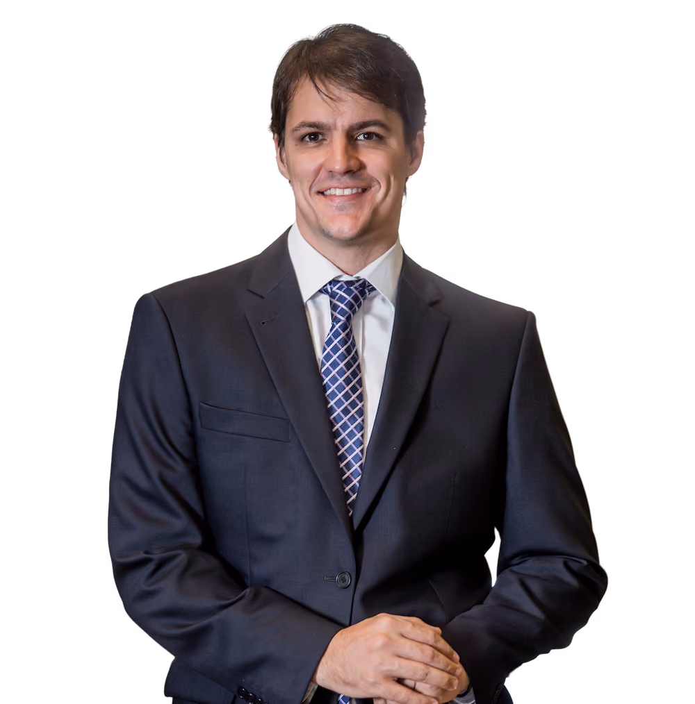 Smiling man in dark suit and patterned tie posing with hands clasped in front.