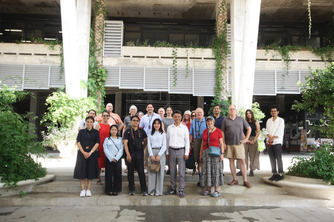 Group of diverse people standing on steps in front of a building with greenery and large white pillars.