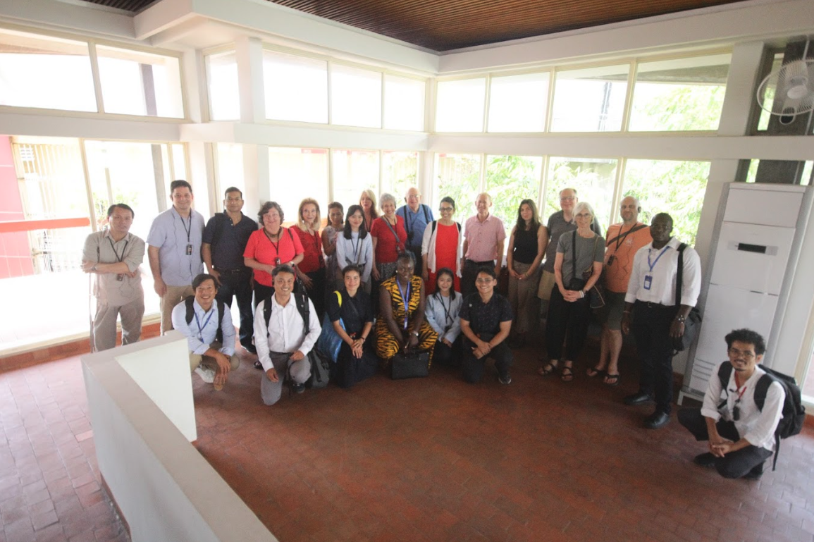 Group of diverse people posing for a photo indoors in a bright room with large windows.