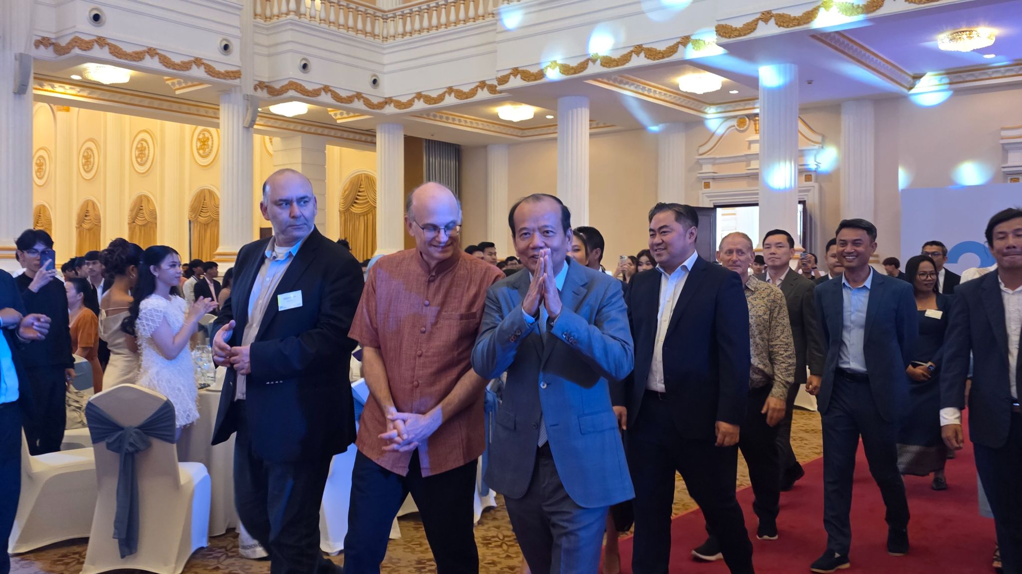 Audience at a panel discussion event on Cambodia's digital future, seated facing a stage with a speaker at a podium and large screens displaying panel information.
