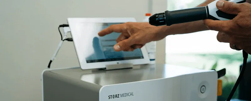 Close-up of a GAINSWave® shockwave therapy device and touchscreen interface used for non-invasive male performance treatments.