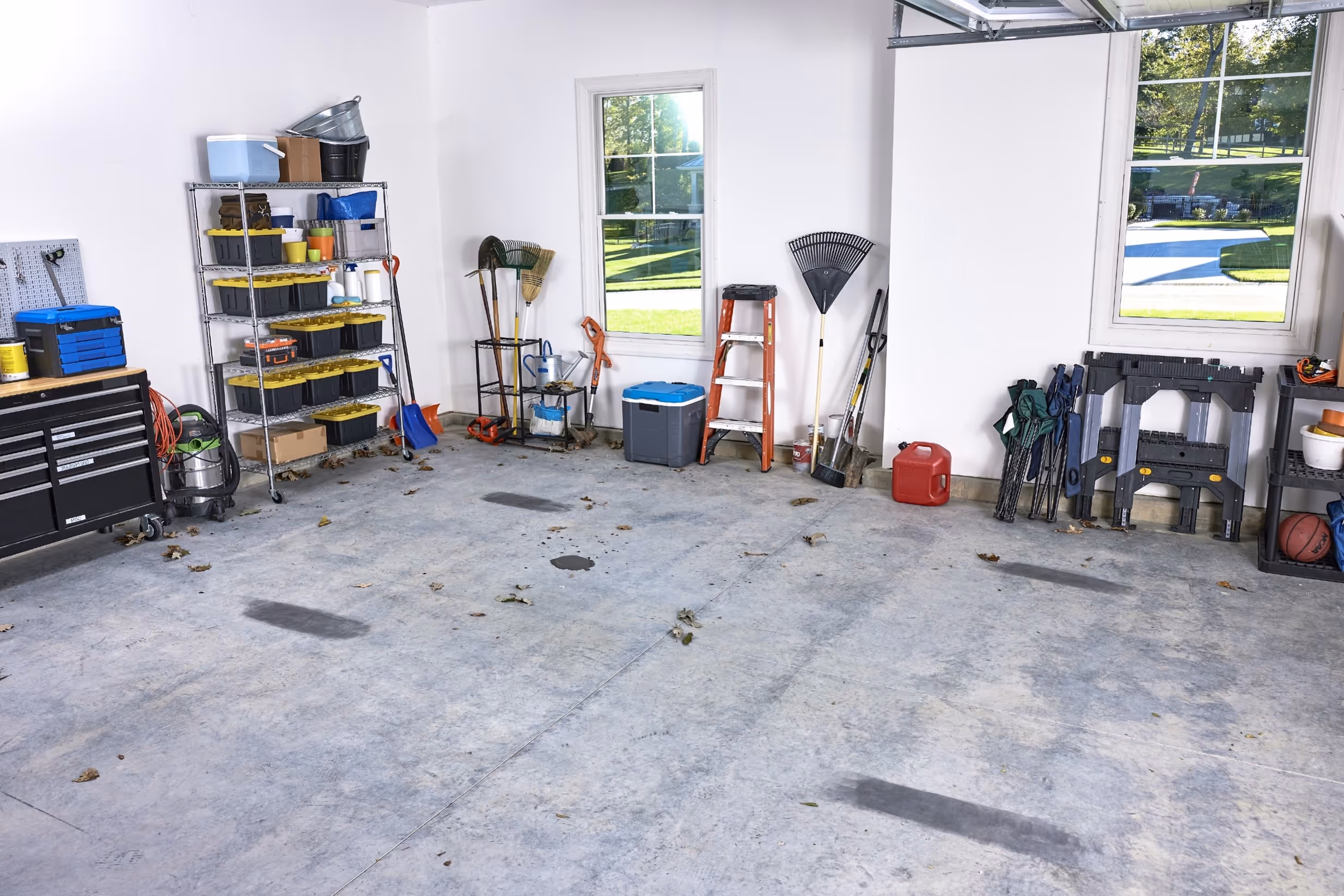 Garage interior with organized shelves holding tools, gardening equipment, ladder, and outdoor gear.