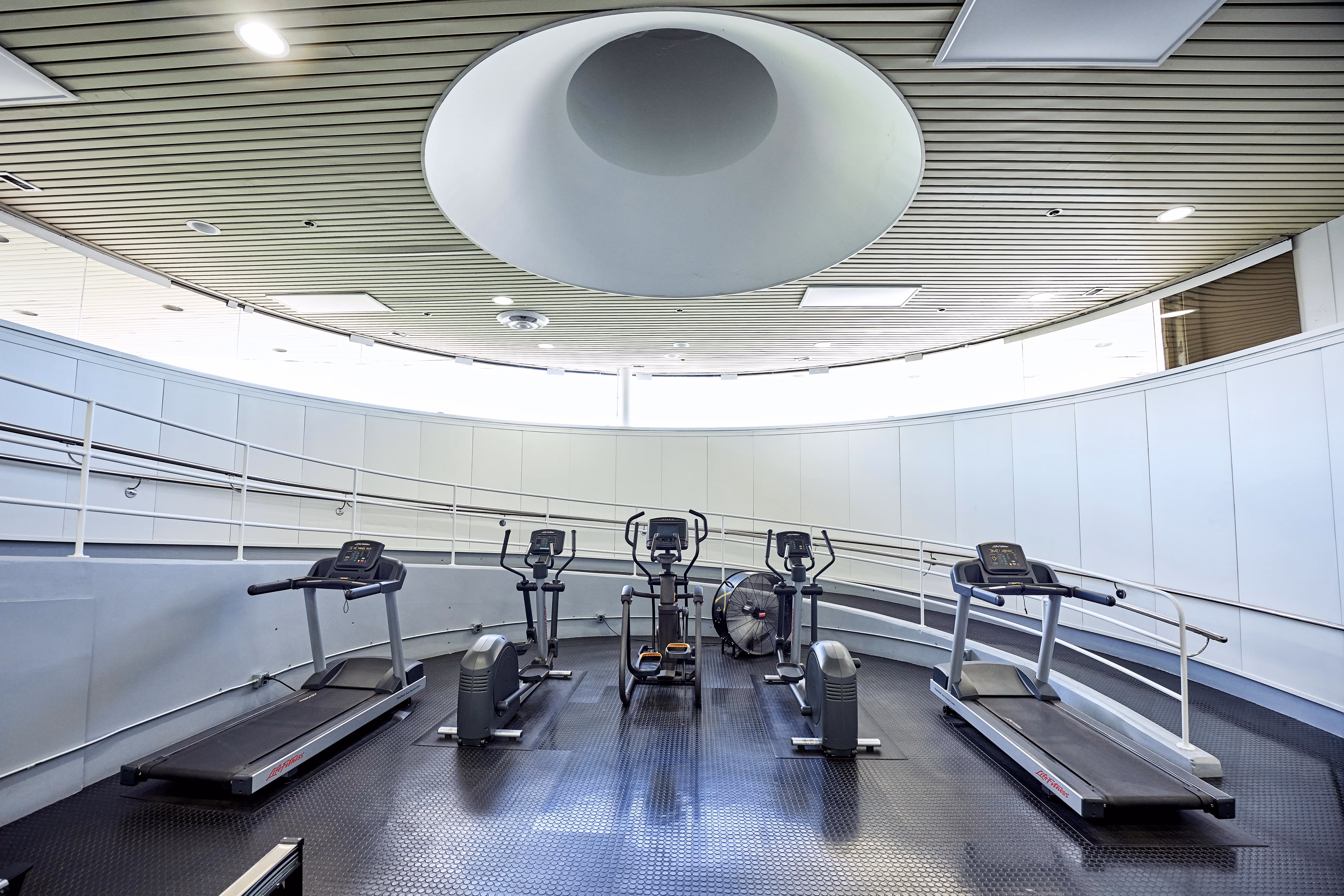 Modern gym room with two treadmills and three elliptical machines under a circular ceiling light.