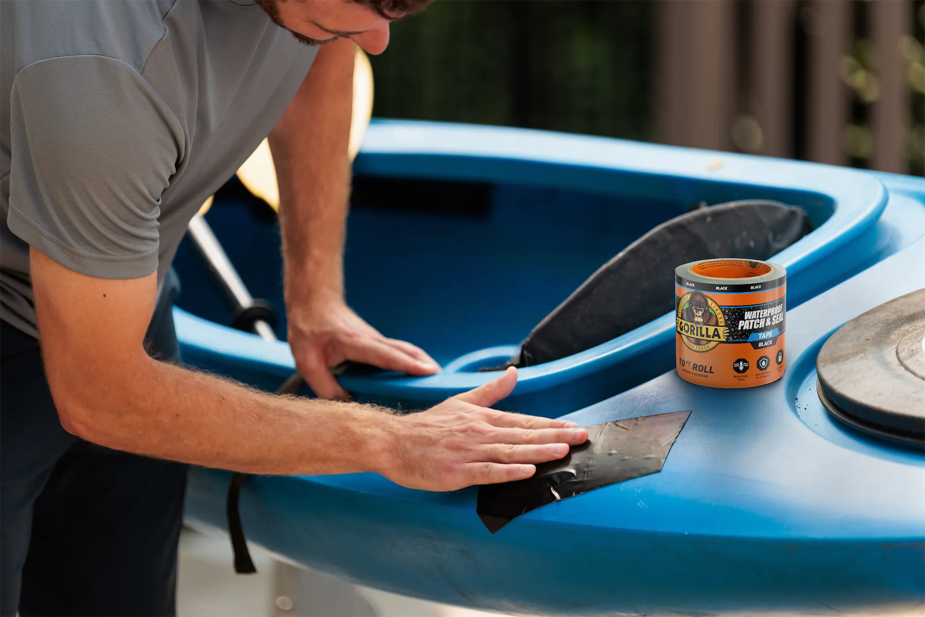Person applying black waterproof patch tape to repair a blue kayak near the paddle.
