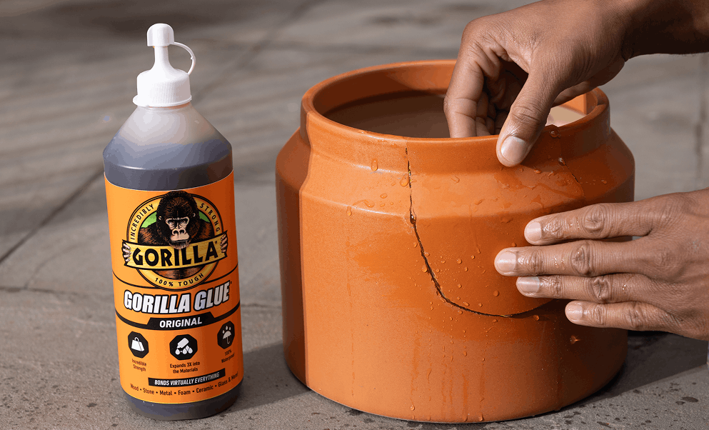 Hands applying Gorilla Glue to repair a large cracked orange ceramic pot.