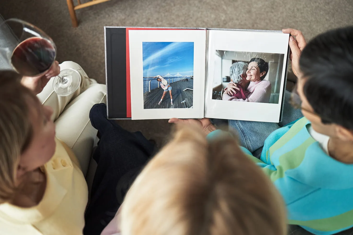 Three people sitting together looking at a photo album featuring a woman stretching outdoors and two women hugging indoors.