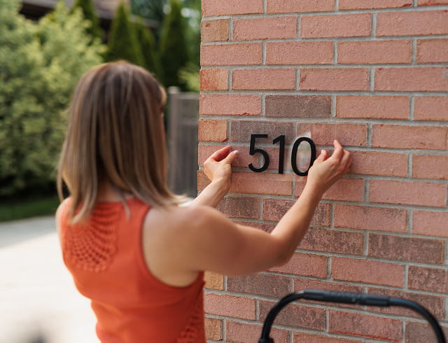 Person placing black house numbers '510' on a red brick wall outdoors.
