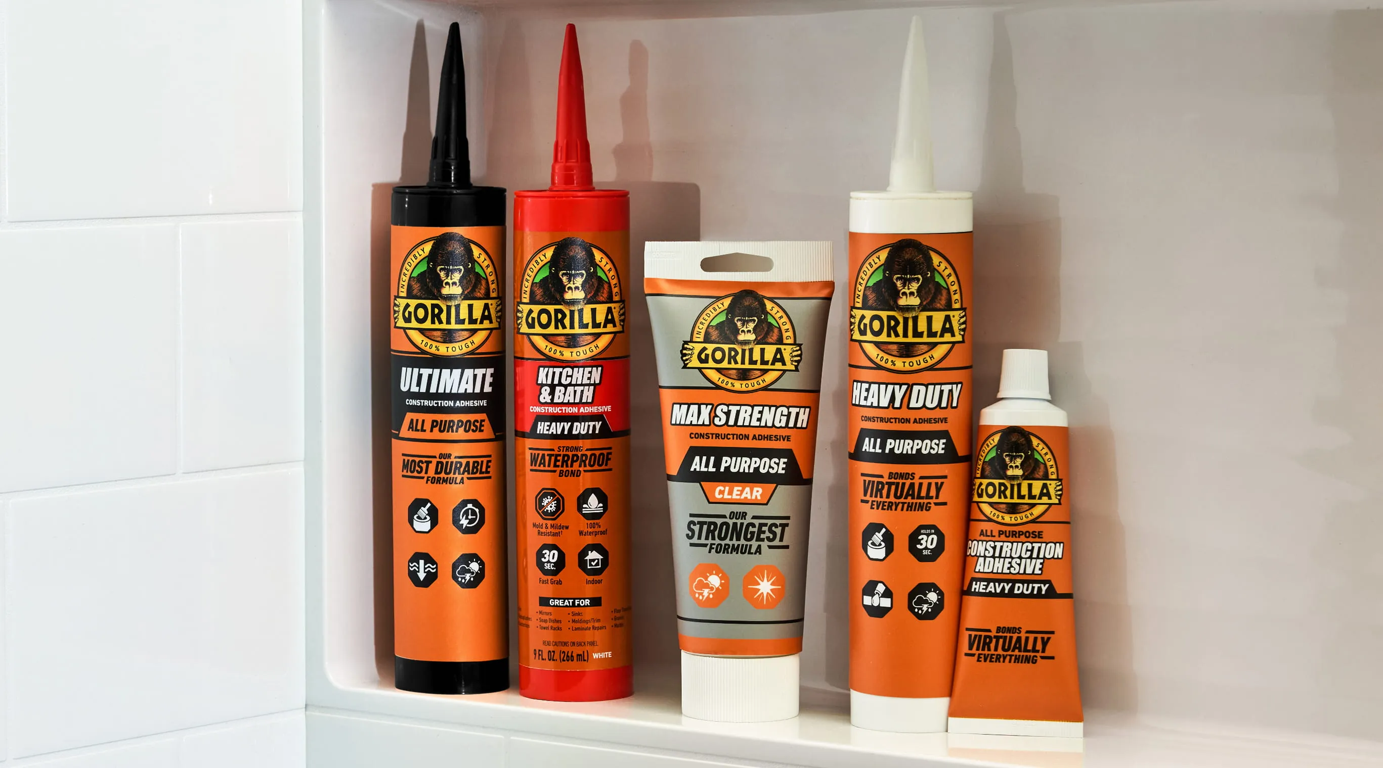 Five Gorilla brand construction adhesive products in various containers, including tubes and squeeze bottles, arranged on a white shelf against a tiled wall.