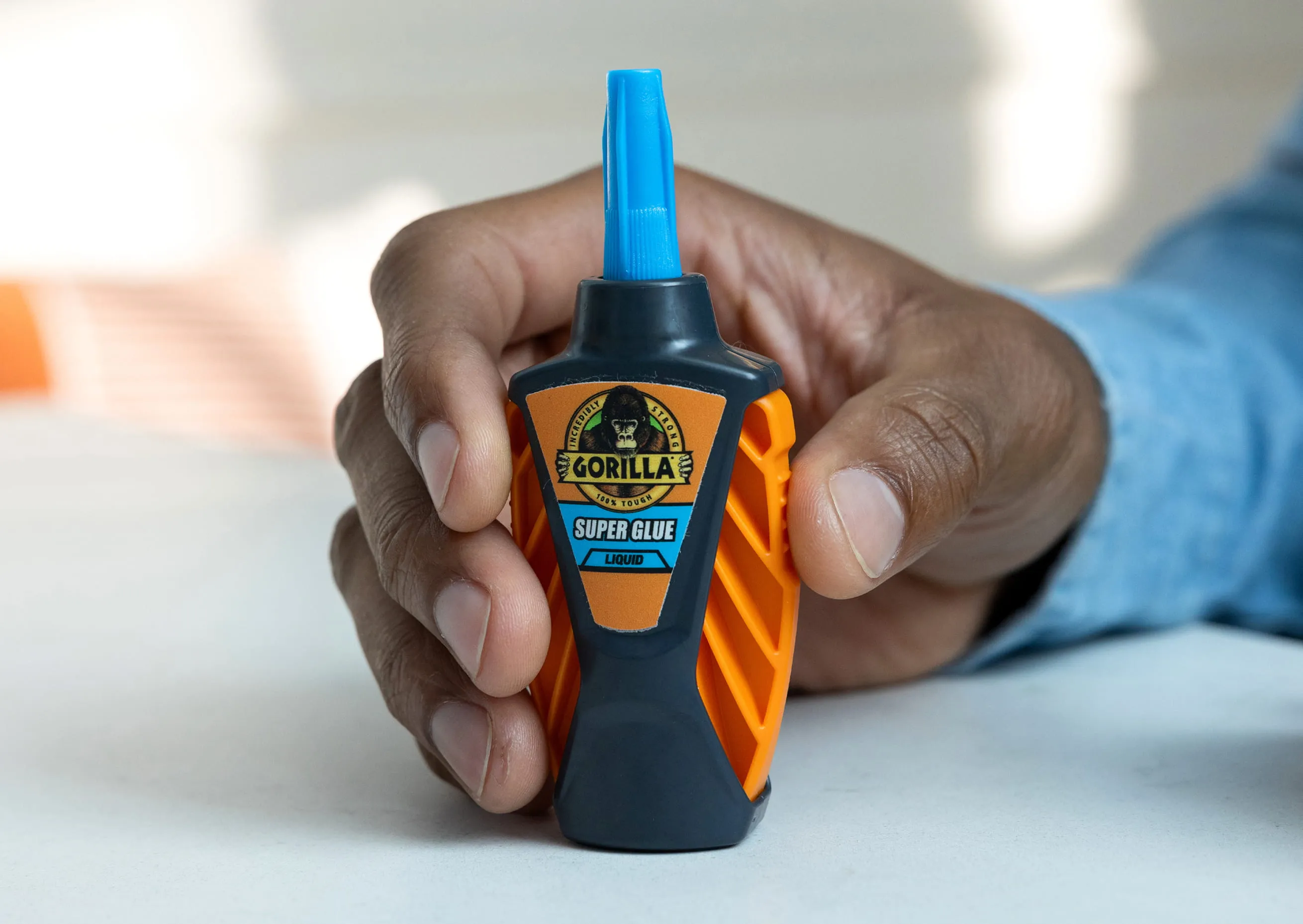 Hand holding a bottle of Gorilla Super Glue Liquid with orange and black packaging.
