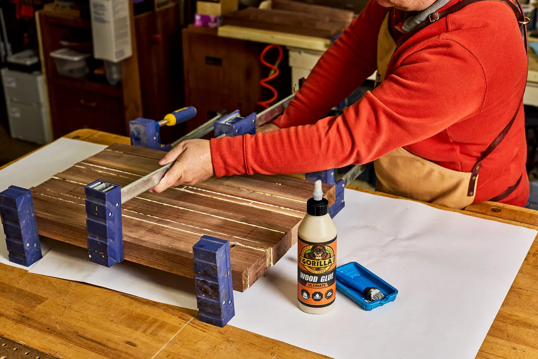 Person clamping glued wood pieces with large bar clamps in a workshop.