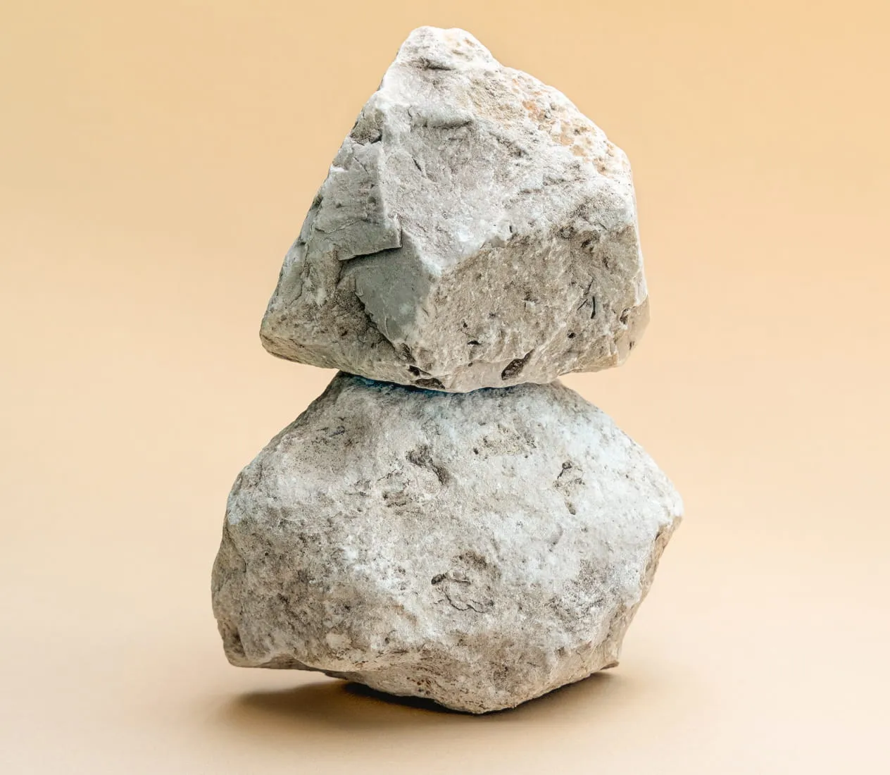 Two rough, gray stones stacked on each other against a beige background.