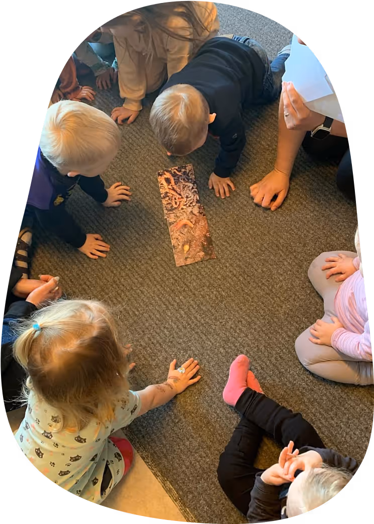 Barn i förskola sitter i ring på golvet och utforskar en bild på maskar under en lärande aktivitet i naturkunskap.