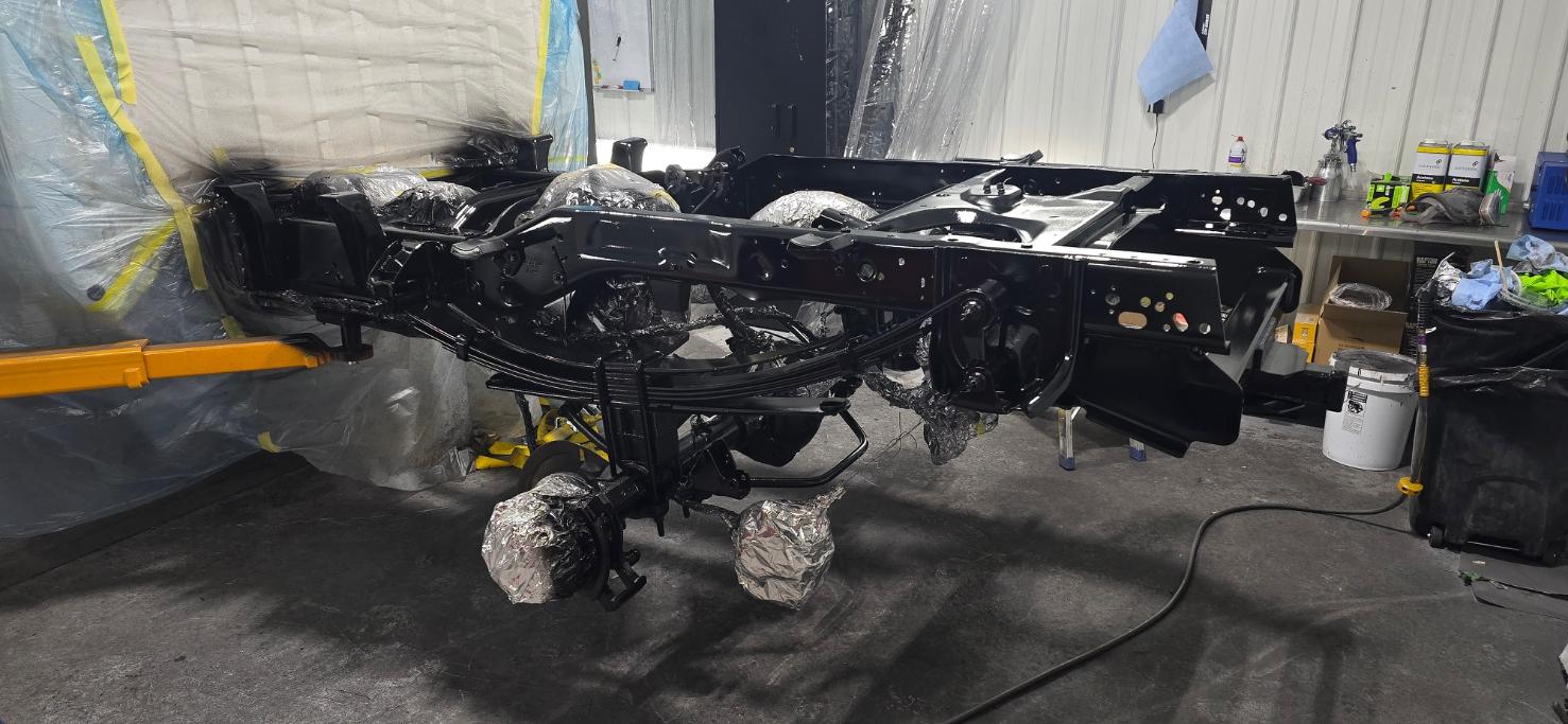 Black-painted truck chassis and frame suspended in a workshop with components wrapped in protective foil.