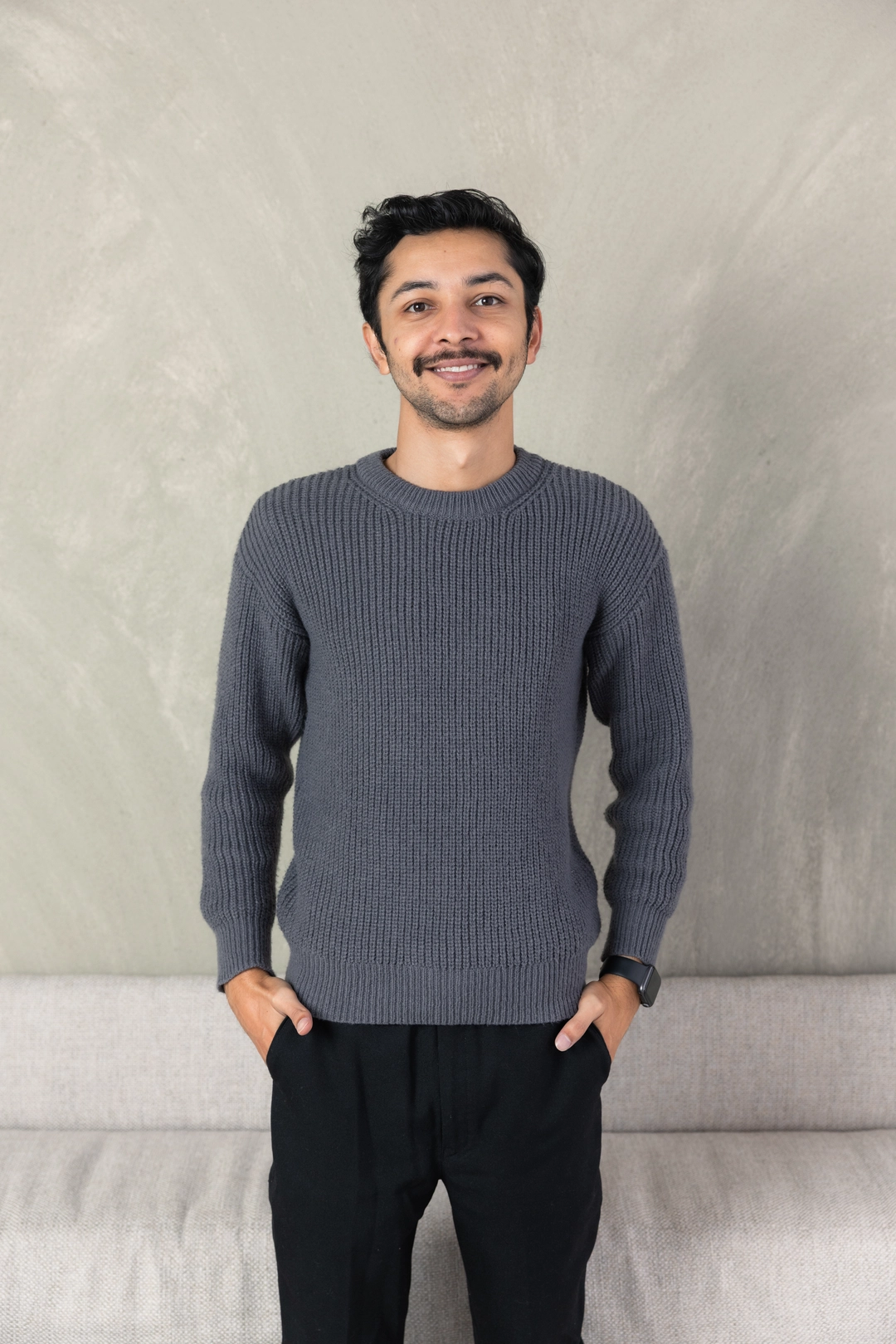 Aman Hirani, Adcraft Studio's website director, against a textured grey studio wall.