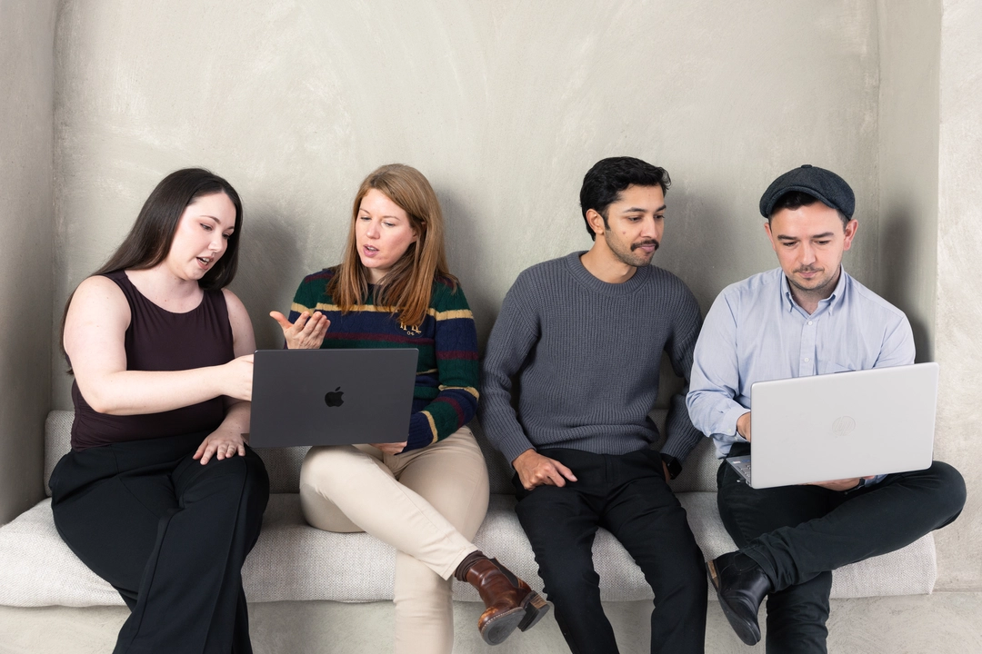 The Adcraft Studio team sitting together on a sofa in their Wollongong studio, reviewing work on two laptops.