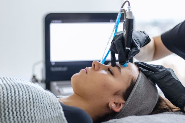 Close-up of a woman receiving a professional facial treatment with a handheld device near her forehead.