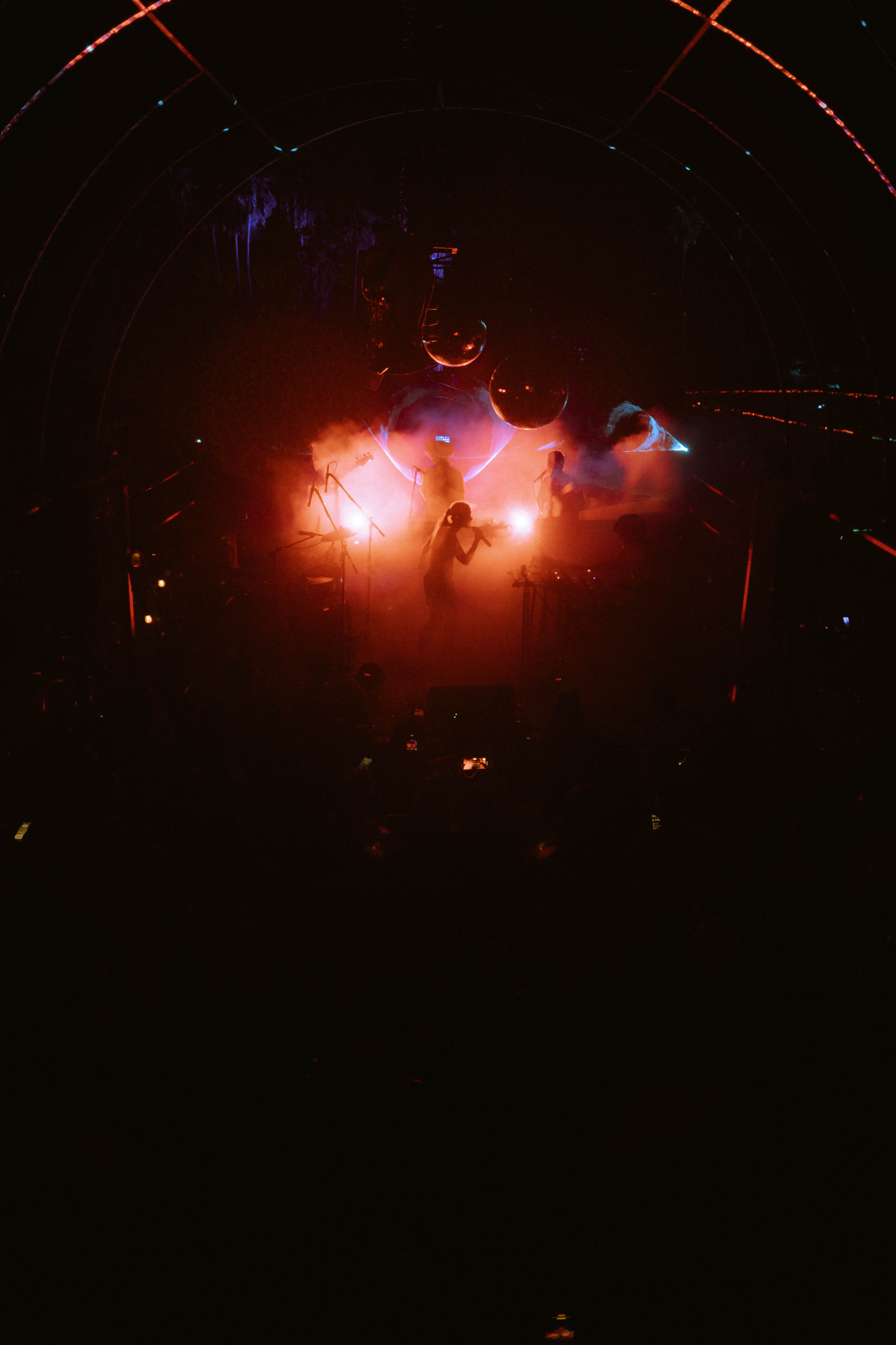Silhouettes of musicians performing on a dimly lit stage with red and blue lights and smoke effects.