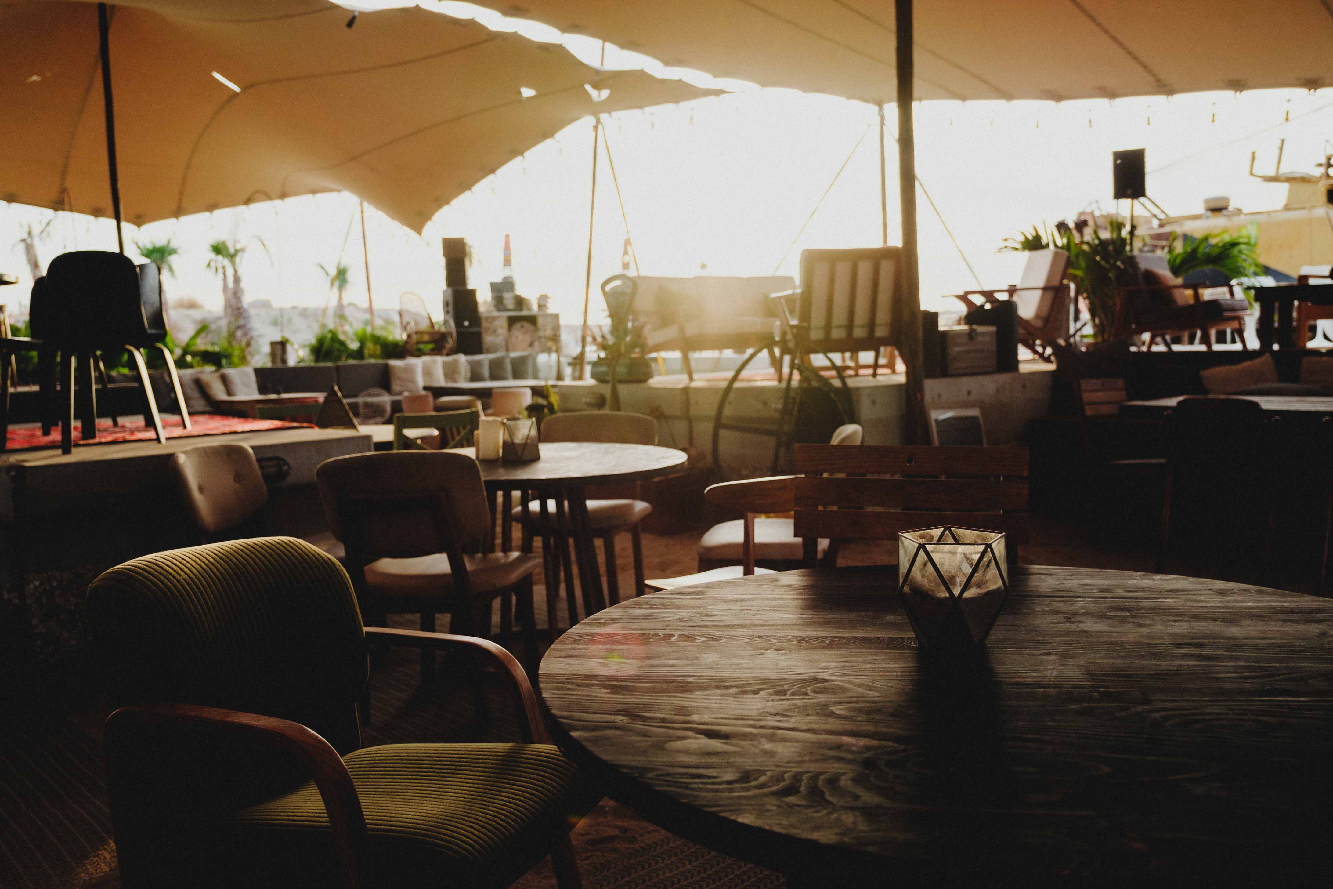 Dimly lit outdoor seating area with wooden tables, various chairs, and large canopy overhead.