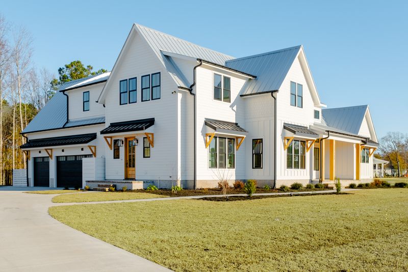 Modern white coastal farmhouse with metal roof, black garage doors, and covered front porch in North Carolina.