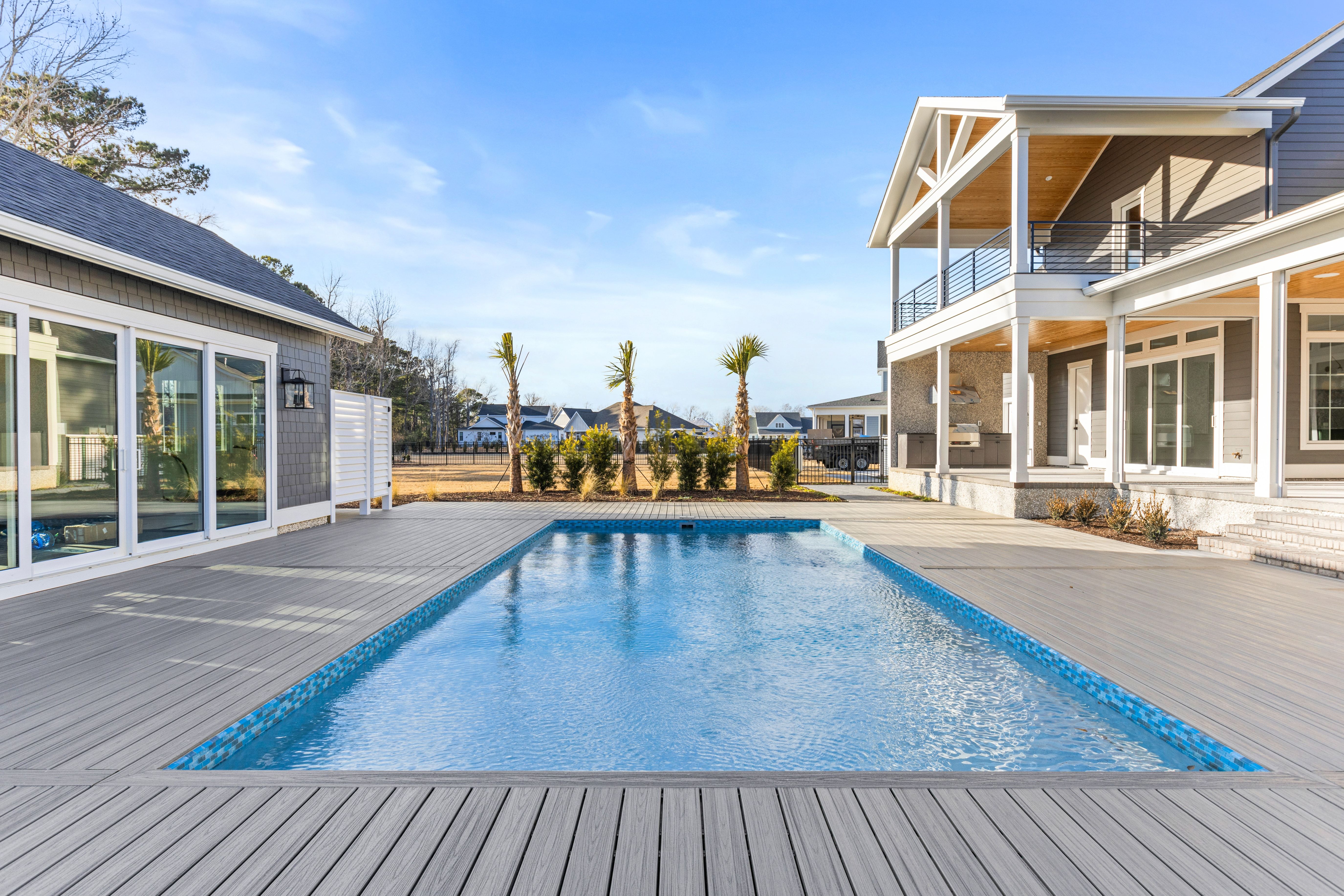 Long pool with a gray deck beside a home with porches, New Port custom home built by Longshore Custom Homes in Hampstead, NC
