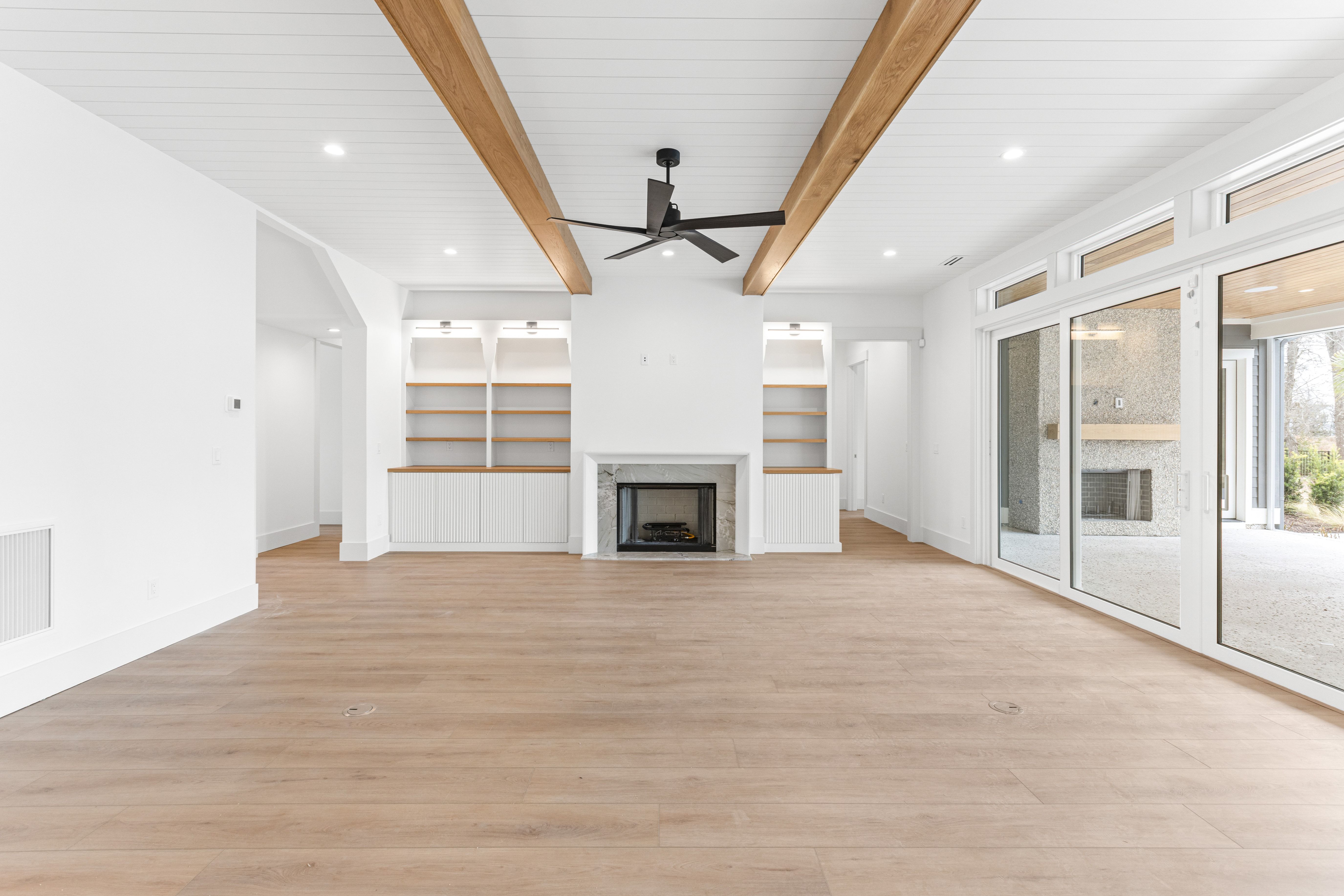 Open living room with wood beams, a fireplace and glass doors in the New Port custom home, Hampstead, NC