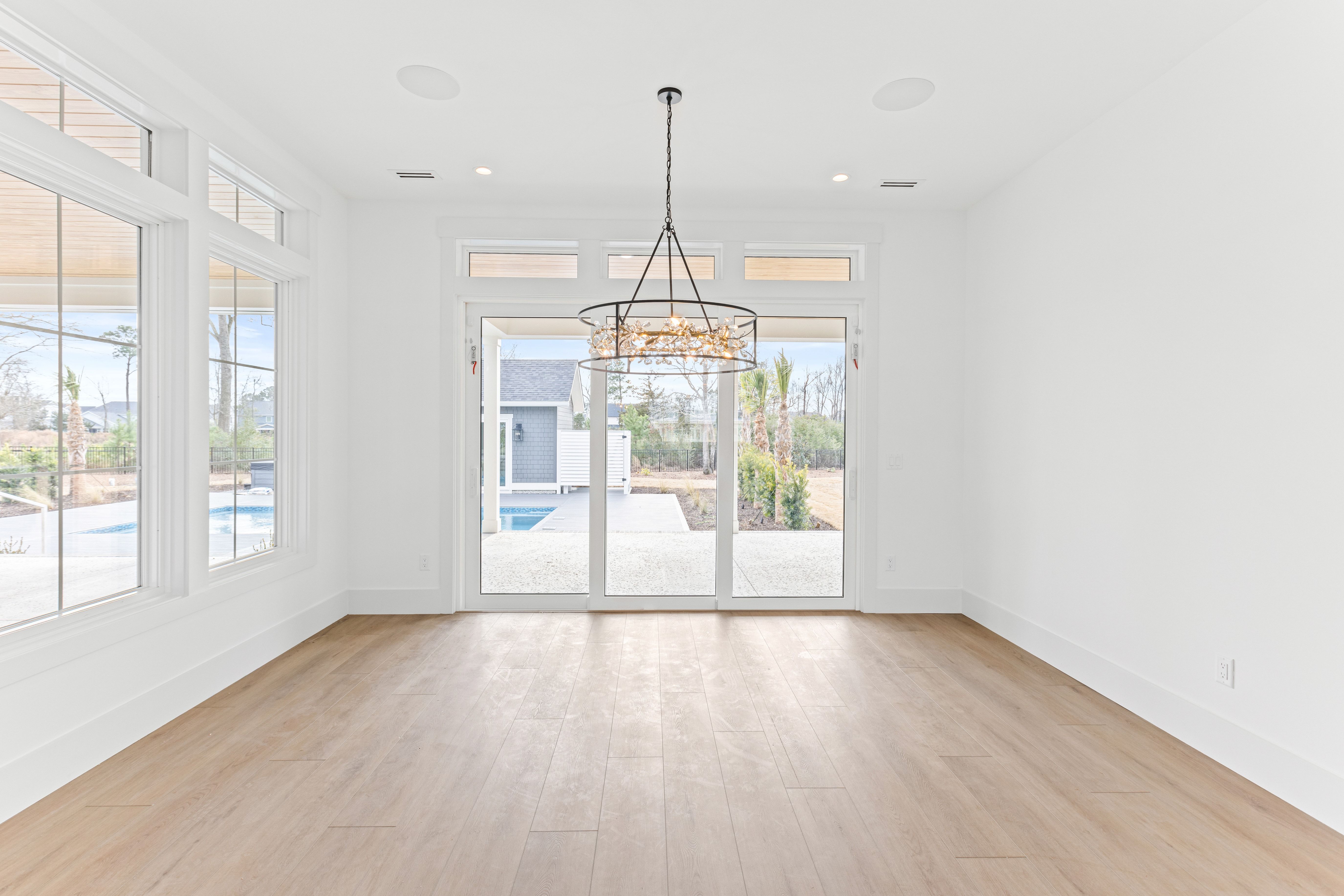 Empty room with a gold chandelier and glass doors to the pool in the New Port custom home, Hampstead, NC