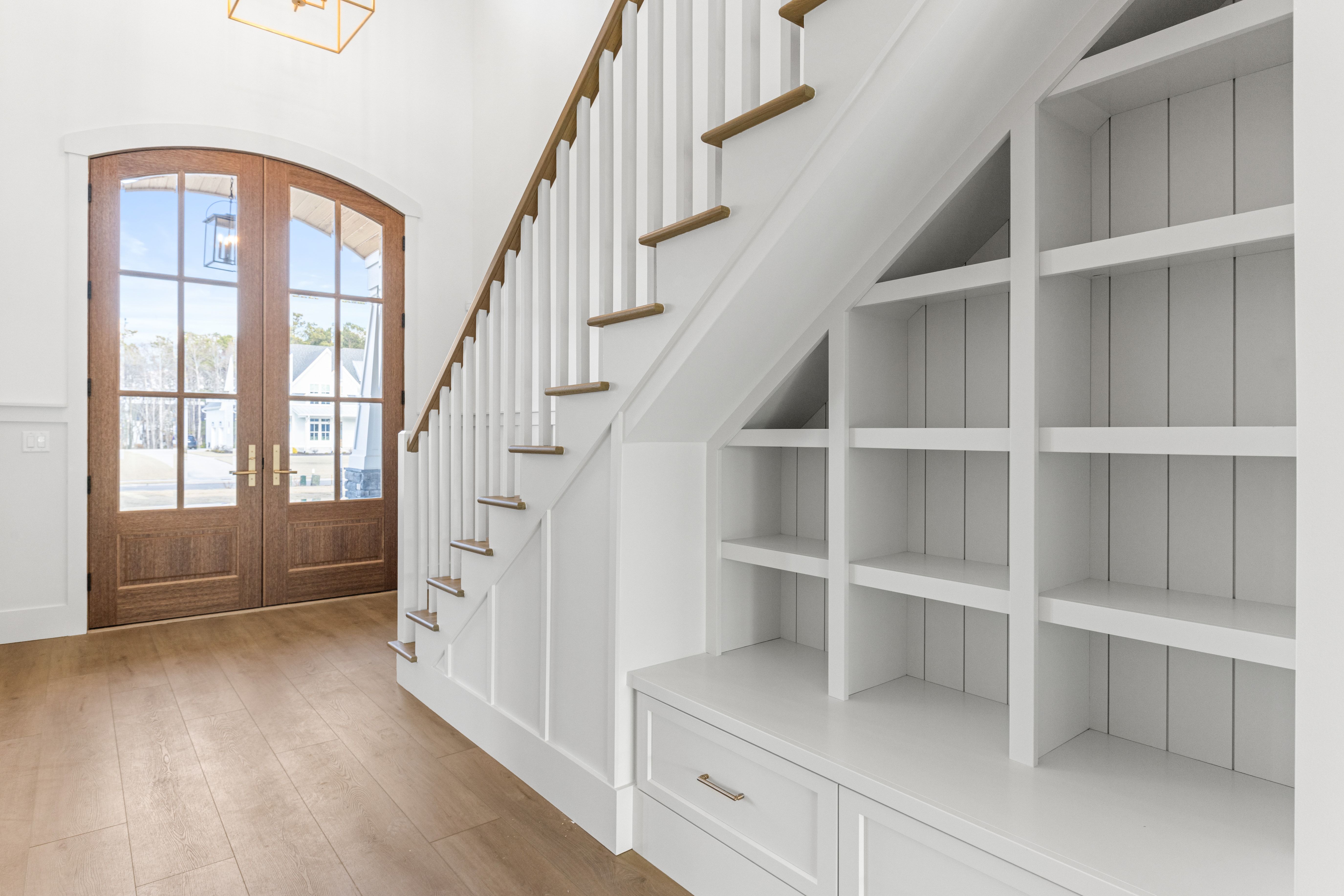 Foyer with arched wood double doors and a staircase with shelves in the New Port custom home, Hampstead, NC