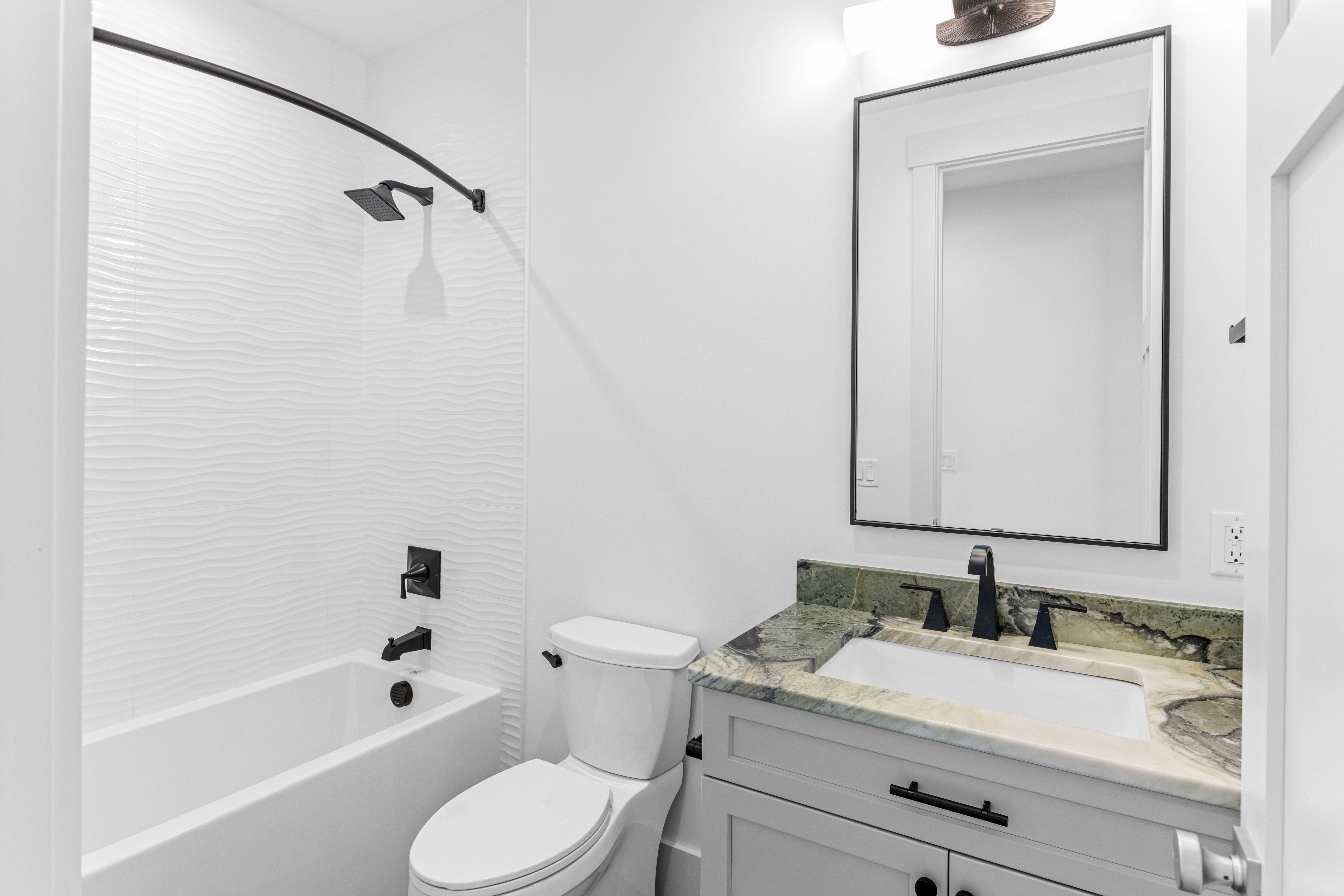 Bathroom with a tub, black mirror and gray vanity with a stone top in the New Port custom home, Hampstead, NC