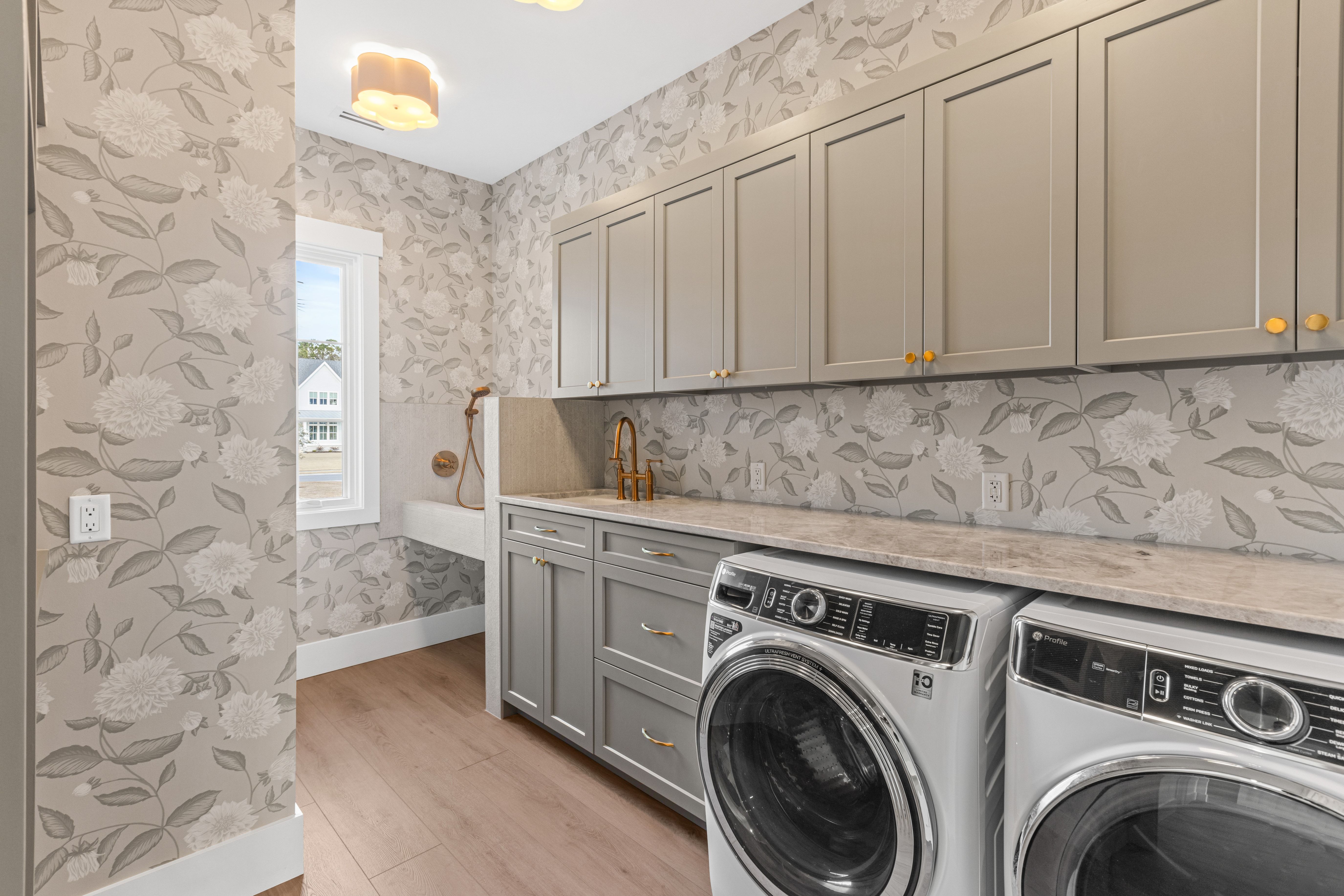 Laundry room with gray cabinets, leaf wallpaper and a washer and dryer in the New Port custom home, Hampstead, NC