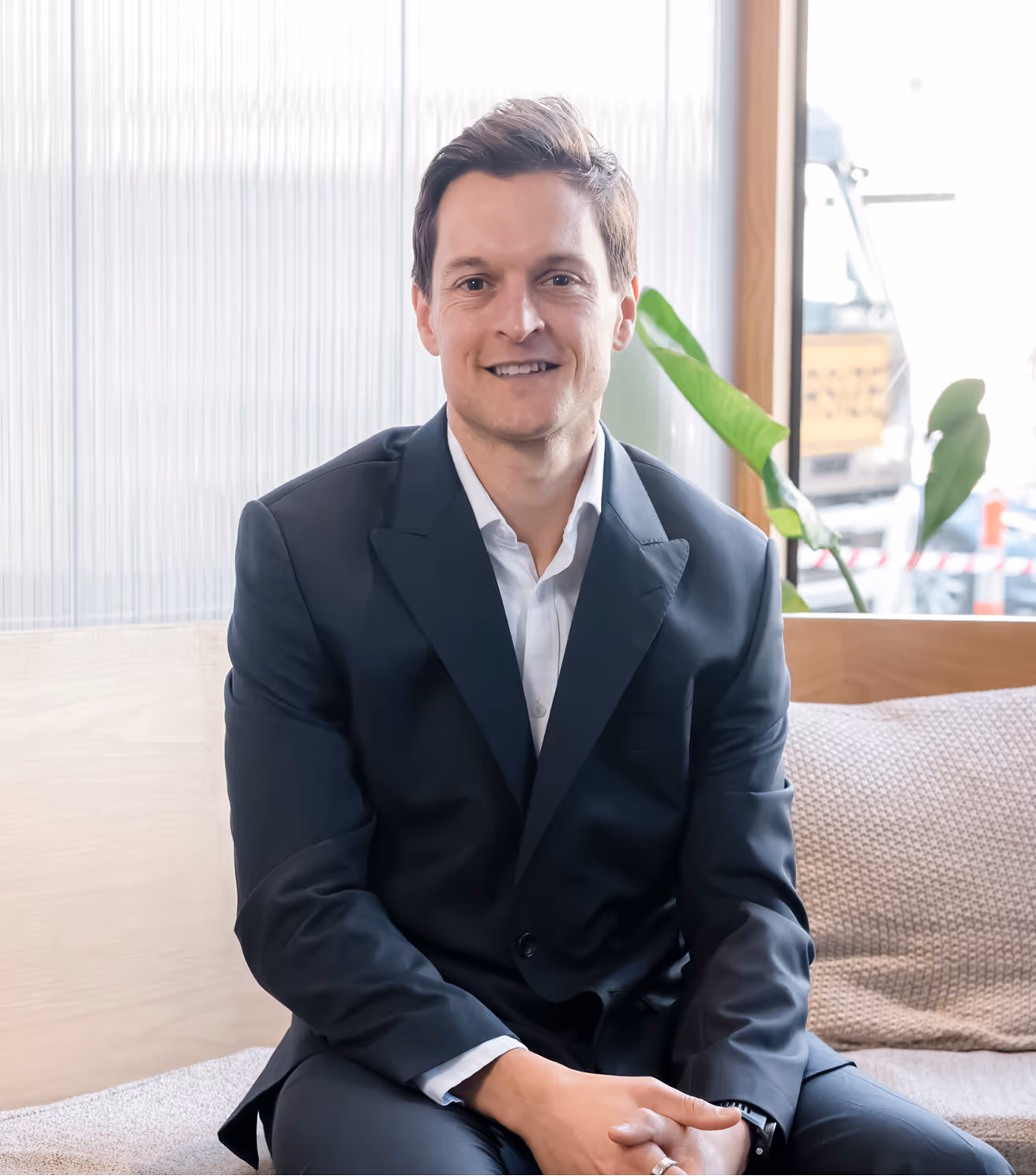 Man in suit sitting on couch, smiling indoors